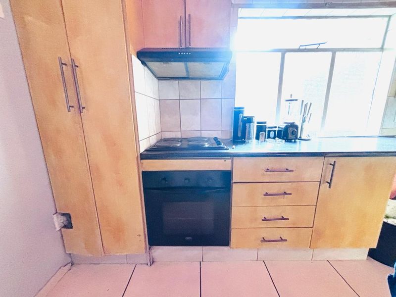 A compact kitchen featuring built-in cabinetry, an electric oven, hob, and extractor fan, with tiled flooring and backsplash.