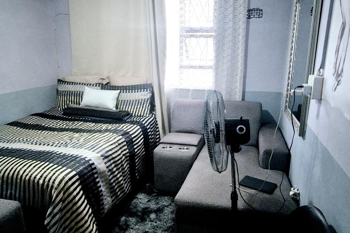 A compact bedroom featuring tiled flooring, a window with security bars, and a central ceiling light fixture.