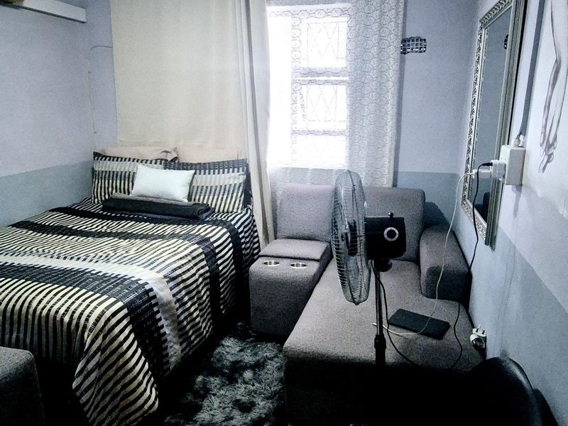A compact bedroom featuring tiled flooring, a window with security bars, and a central ceiling light fixture.