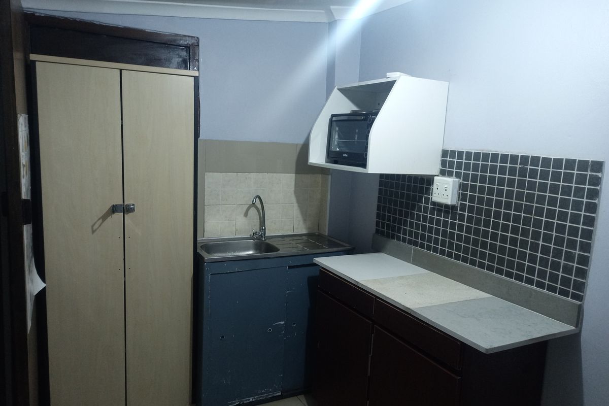A compact kitchen area featuring a stainless steel sink, tiled backsplash, and built-in cabinetry with a dedicated cupboard space.