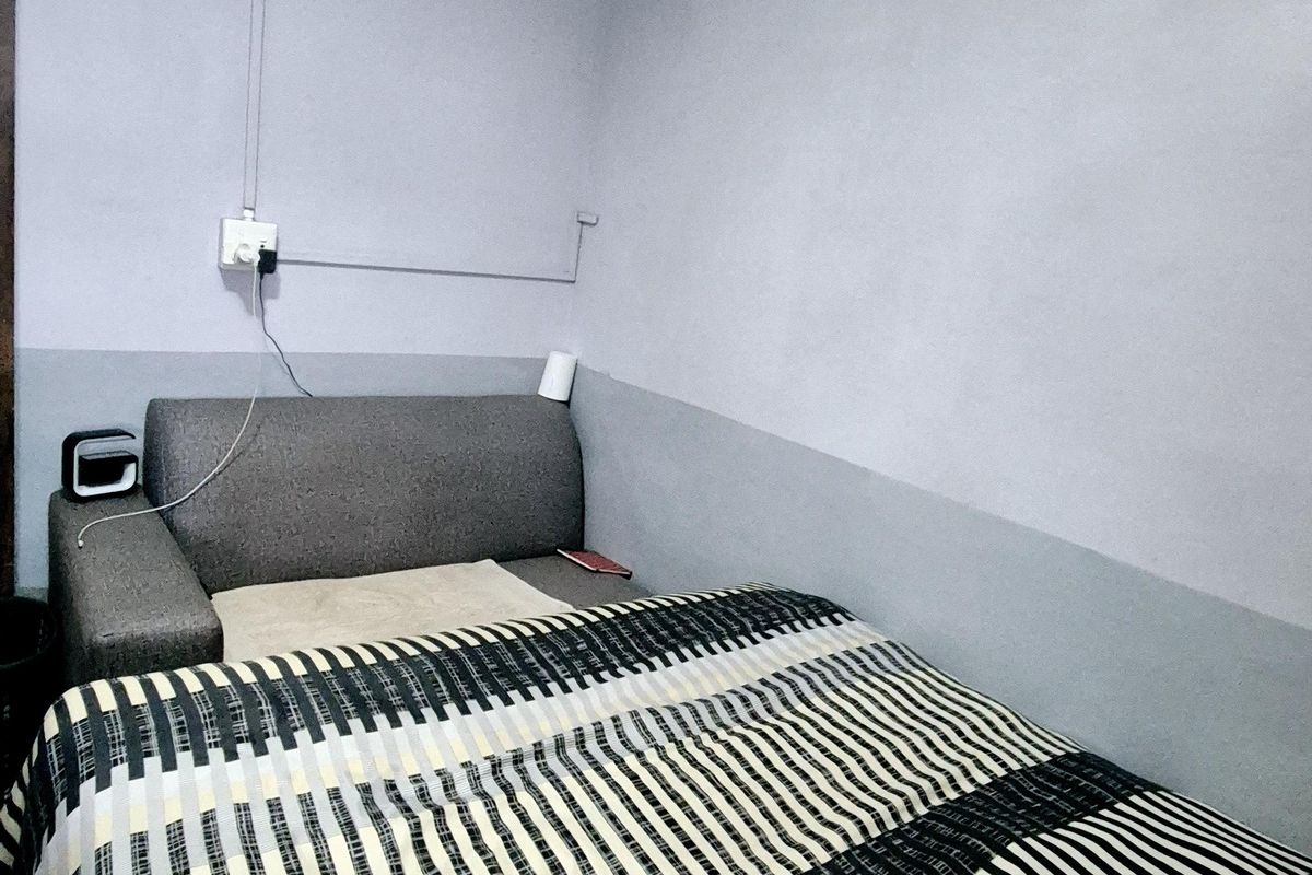 A compact bedroom featuring a wall-mounted split-system air conditioner and surface-mounted electrical wiring.