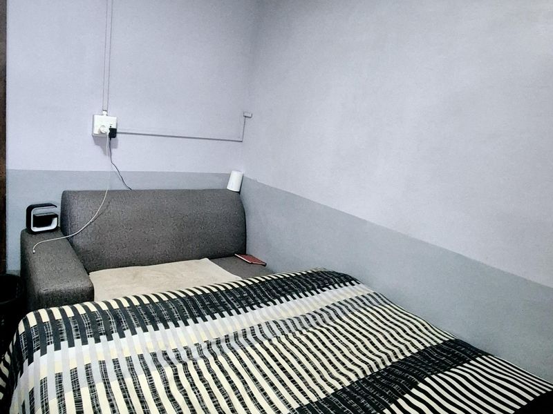 A compact bedroom featuring a wall-mounted split-system air conditioner and surface-mounted electrical wiring.