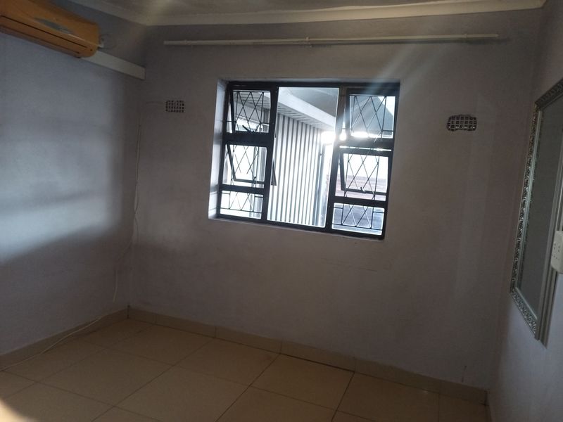 An empty bedroom featuring tiled flooring, security bars on the window, and a wall-mounted air conditioning unit.