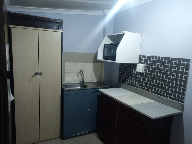A compact kitchen area featuring a stainless steel sink, tiled backsplash, and built-in cabinetry with a dedicated cupboard space.