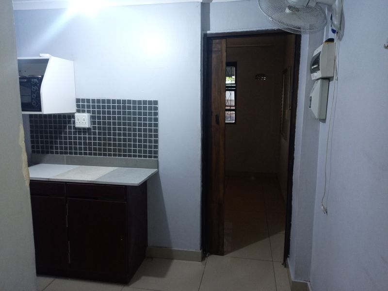 A compact kitchen area featuring built-in cabinetry, a tiled backsplash, and direct access to an adjacent room.