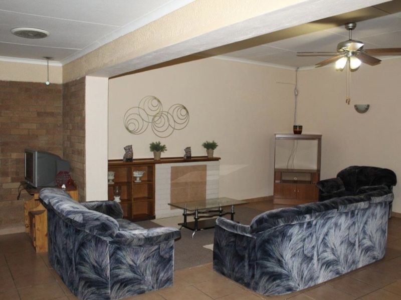 Spacious living room featuring a brick accent wall, tiled flooring, and a ceiling fan, offering a comfortable and functional layout.