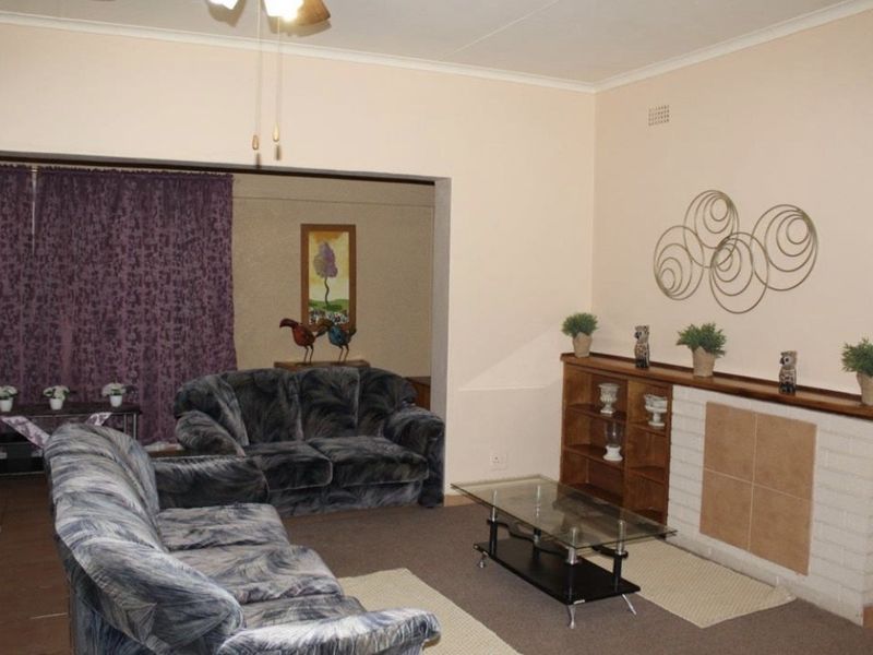 A living room featuring a brick fireplace with a tiled hearth and a ceiling fan, connected to an adjacent living space.