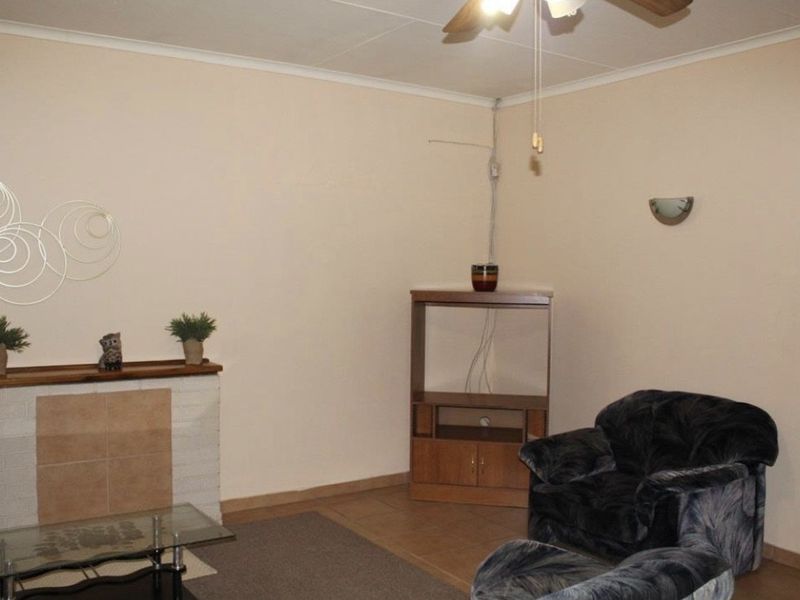 A living room featuring a tiled fireplace, ceiling fan, and tiled flooring, requiring minor cosmetic updates and electrical tidying.
