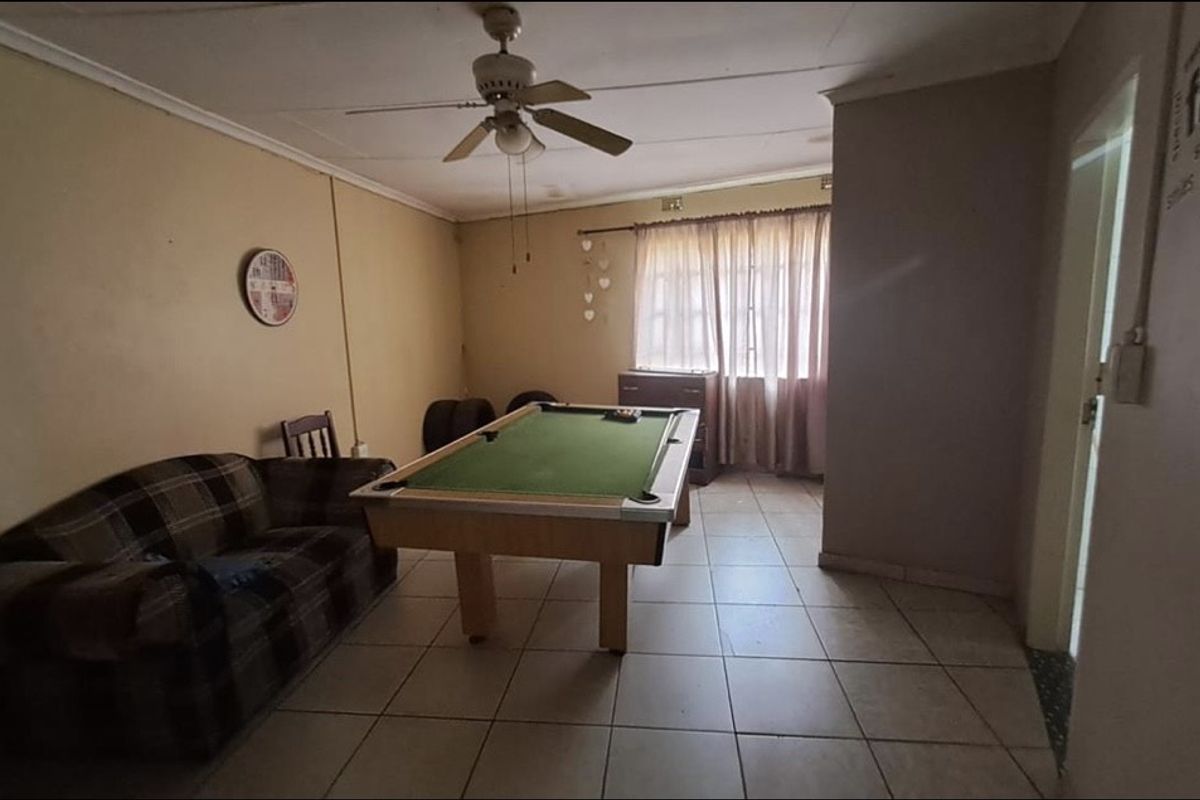 A living area featuring tiled flooring and a ceiling fan, currently utilized as a recreational space.