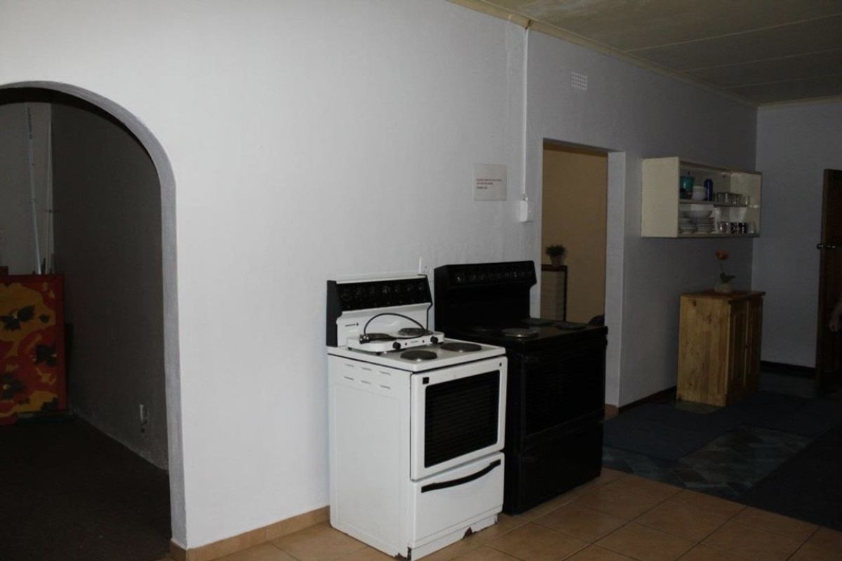 A basic kitchen area featuring tiled flooring, an arched entryway, and wall-mounted shelving, currently presenting as a functional but dated space.