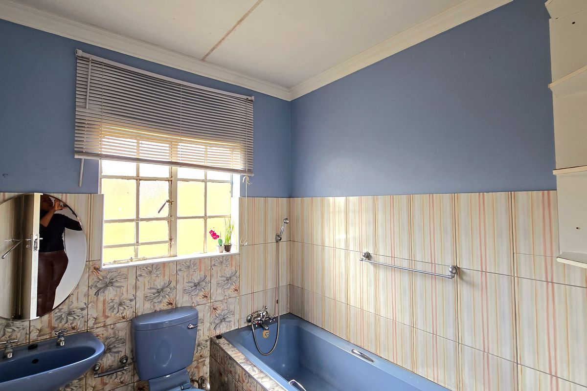 A dated bathroom featuring blue sanitaryware, tiled walls, and a built-in bathtub, offering significant potential for a modern renovation.