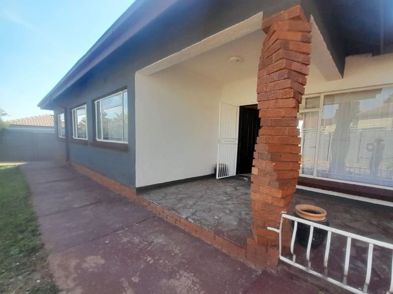 A covered patio area featuring a distinctive brick pillar, stone flooring, and security gate access to the home's interior.