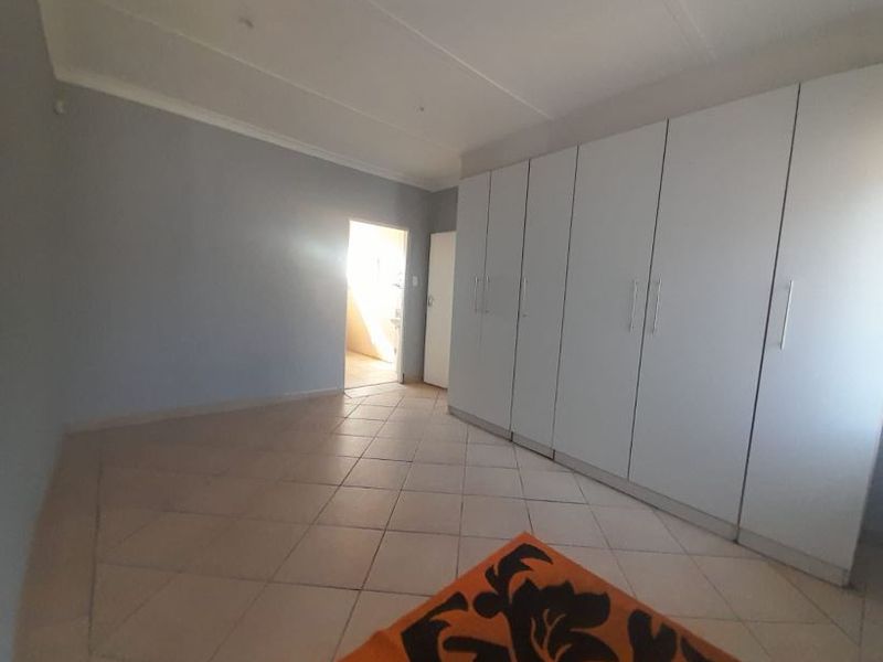 A spacious bedroom featuring neutral walls, tiled flooring, and extensive built-in cupboard storage.