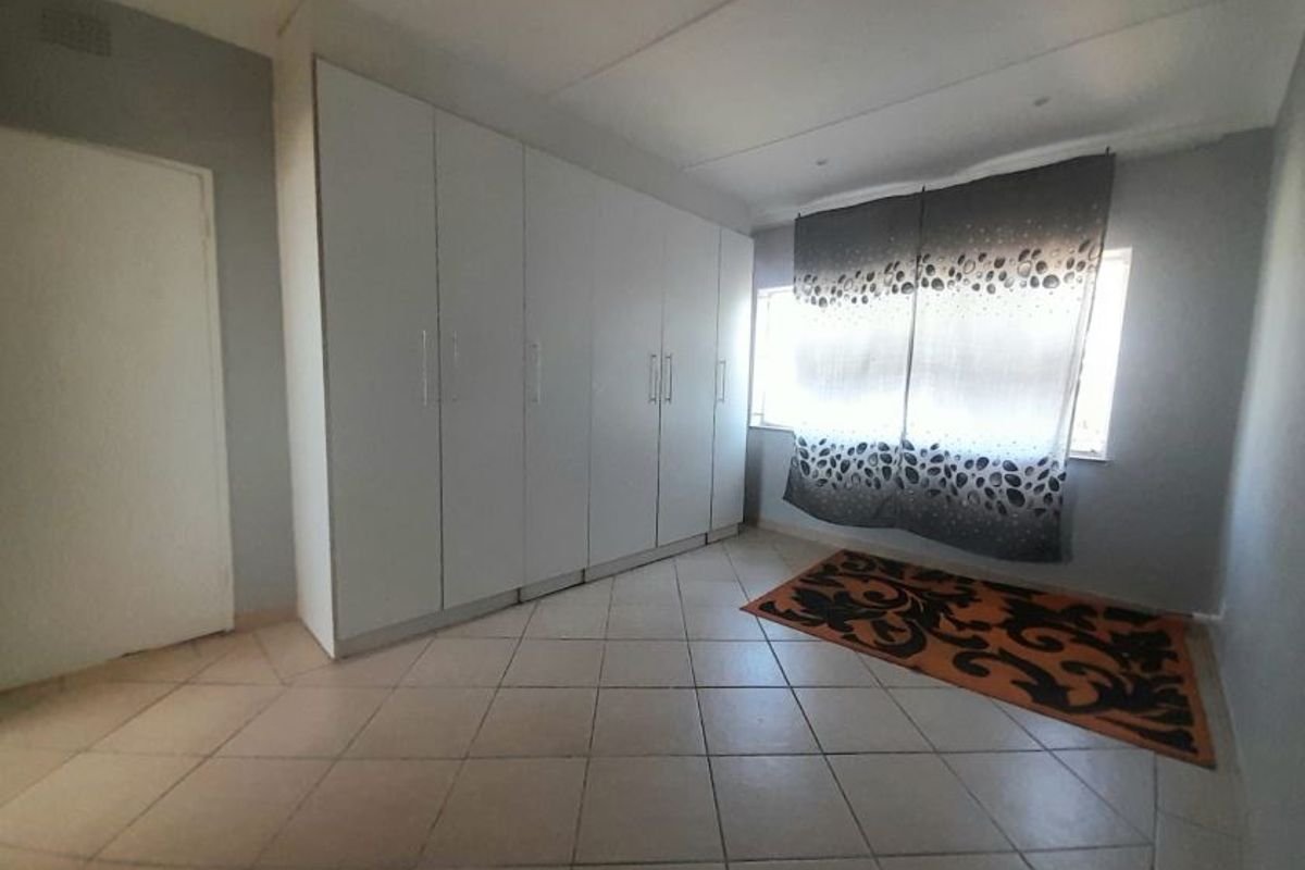 A spacious bedroom featuring neutral wall tones, large built-in cupboards for storage, and durable tiled flooring throughout.