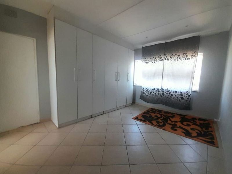 A spacious bedroom featuring neutral wall tones, large built-in cupboards for storage, and durable tiled flooring throughout.