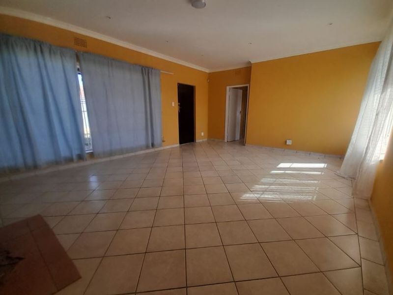 A spacious, empty living room featuring neutral ceramic floor tiles, recessed lighting, and a tiled fireplace hearth, ready for personalization.
