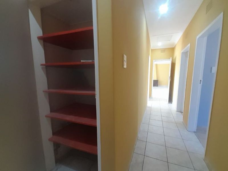 A functional hallway featuring tiled flooring, recessed lighting, and a built-in storage cupboard with open shelving.