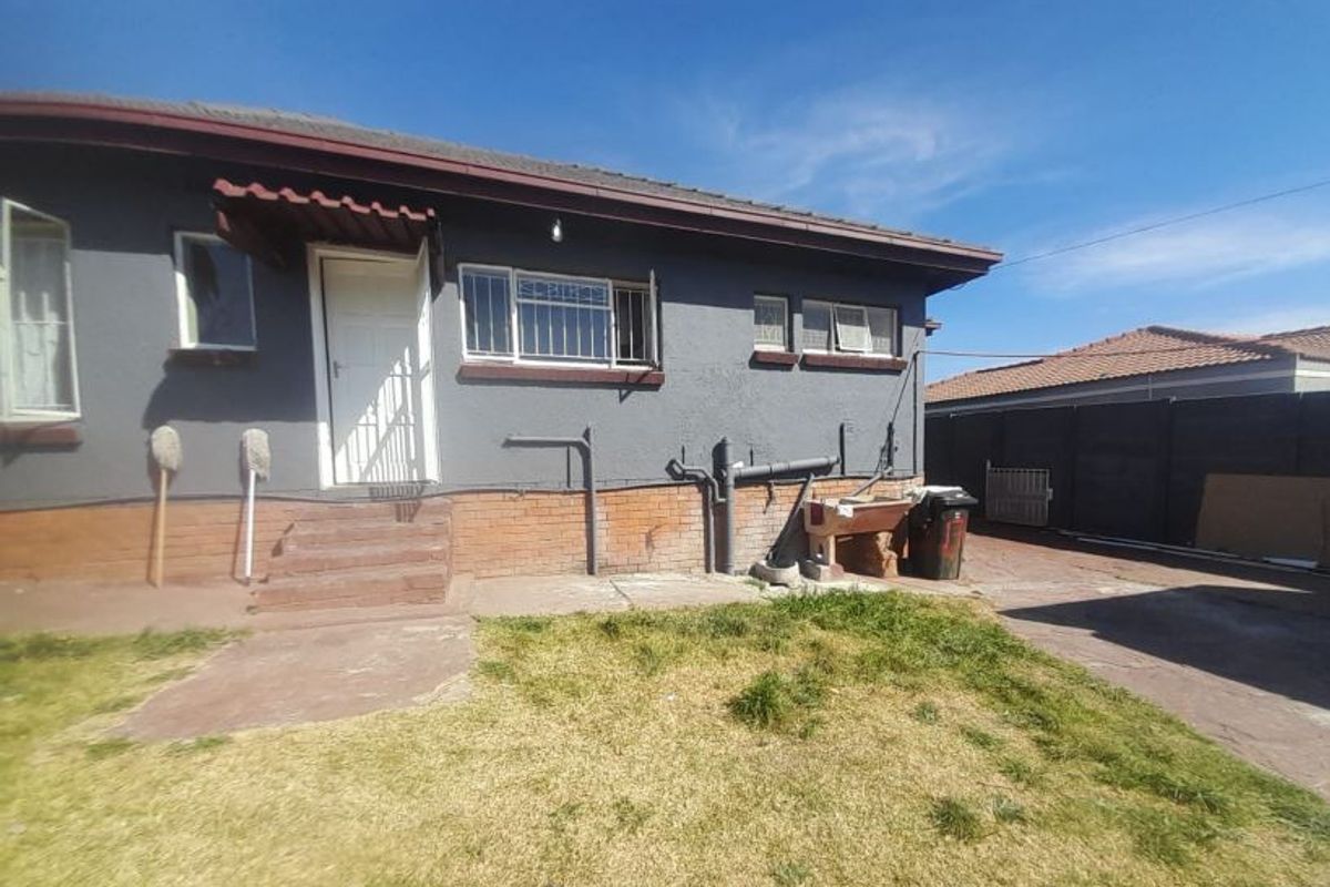 Rear exterior view of the house featuring a brick foundation, security bars on windows, and an exposed concrete apron area.