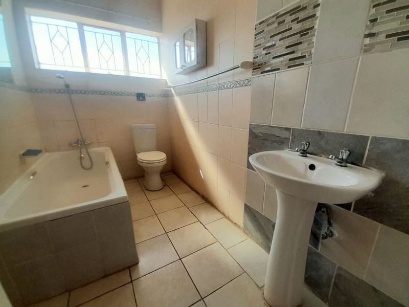 A functional bathroom featuring a bathtub, pedestal basin, and toilet, finished with neutral wall and floor tiling.