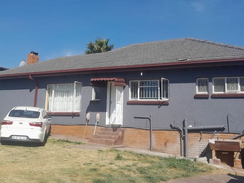 Front elevation of a single-story house featuring a tiled roof, brick plinth, and security bars on windows.