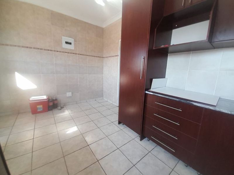 A functional scullery area featuring dark wood built-in cabinetry, tiled walls, and tiled flooring, providing ample storage and workspace.
