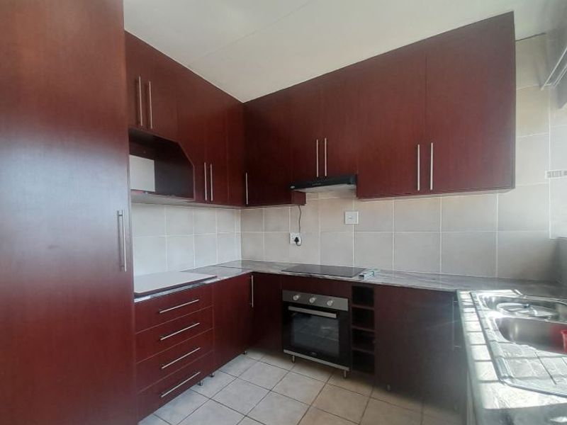 A functional kitchen featuring dark wood cabinetry, laminate countertops, a built-in oven with hob, extractor fan, and tiled finishes throughout.