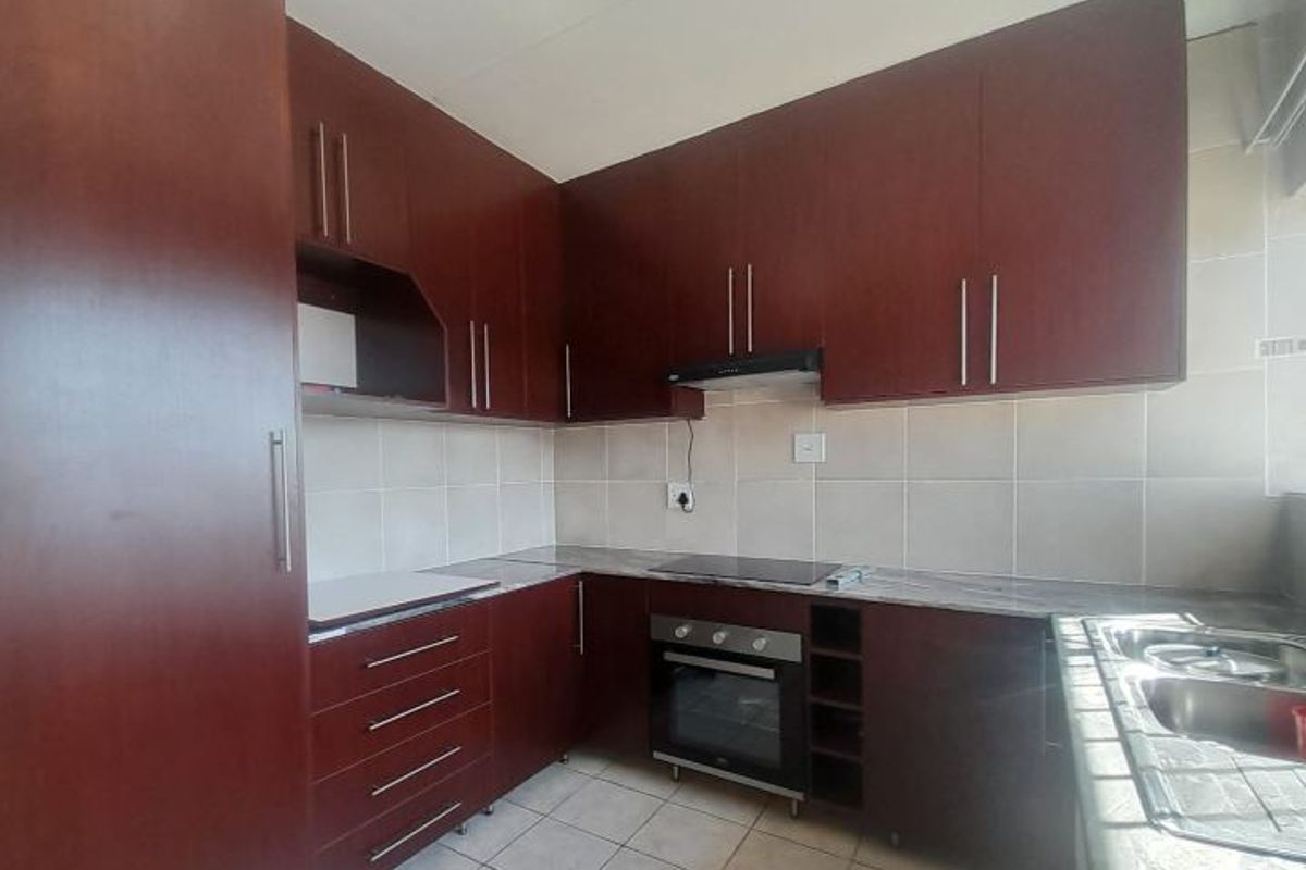 A functional kitchen featuring dark wood cabinetry, laminate countertops, a built-in oven with hob, extractor fan, and tiled finishes throughout.