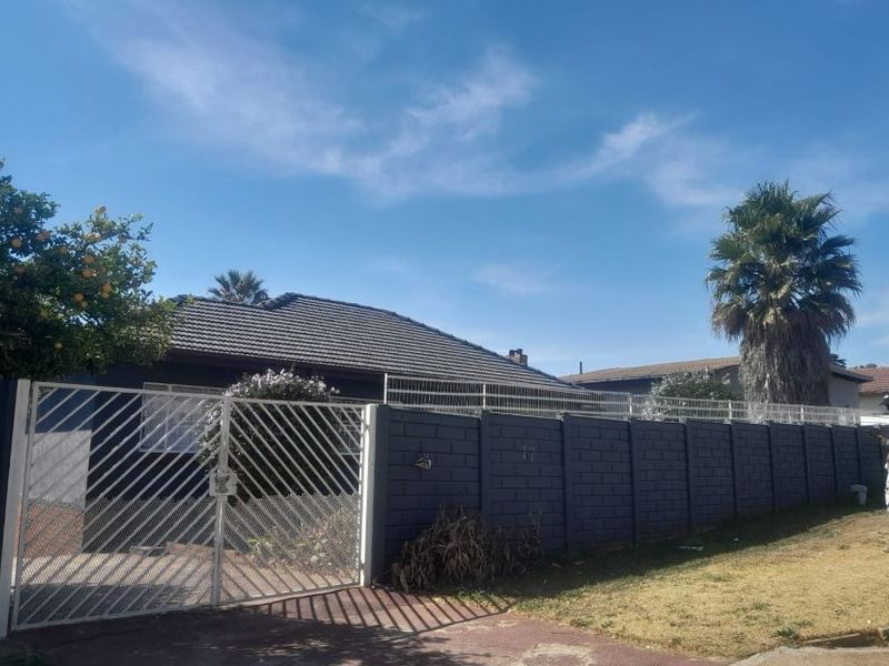 Front view of the property featuring a concrete block boundary wall, metal security gate, and tiled roof structure.