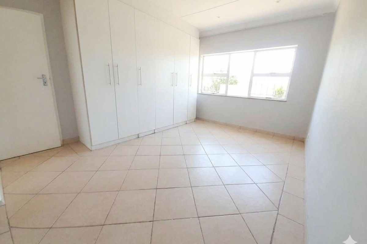 A bright, empty bedroom featuring neutral tiled flooring and extensive built-in cupboard storage space.