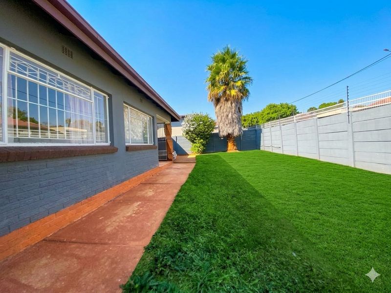 A rear garden area featuring a well-maintained lawn, paved walkway, and secure perimeter walling with electric fencing.