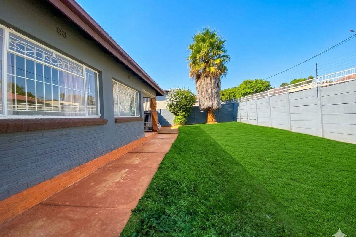 A rear garden area featuring a well-maintained lawn, paved walkway, and secure perimeter walling with electric fencing.