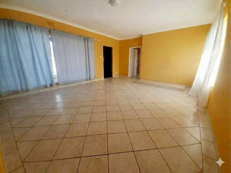 A spacious, empty living room featuring neutral tiled flooring, coved ceilings, and a built-in raised platform area.