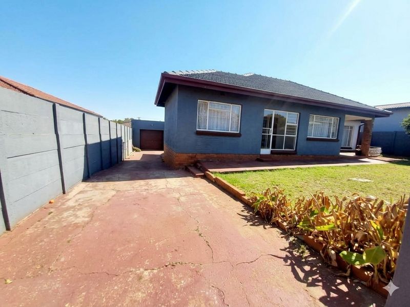 Front view of a single-story house featuring a tiled roof, concrete driveway, and a detached garage, set within a fenced property boundary.
