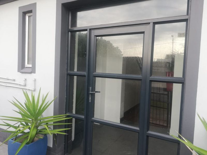Modern entrance featuring a dark grey aluminium frame glass door with a matching transom window and clean exterior finishes.