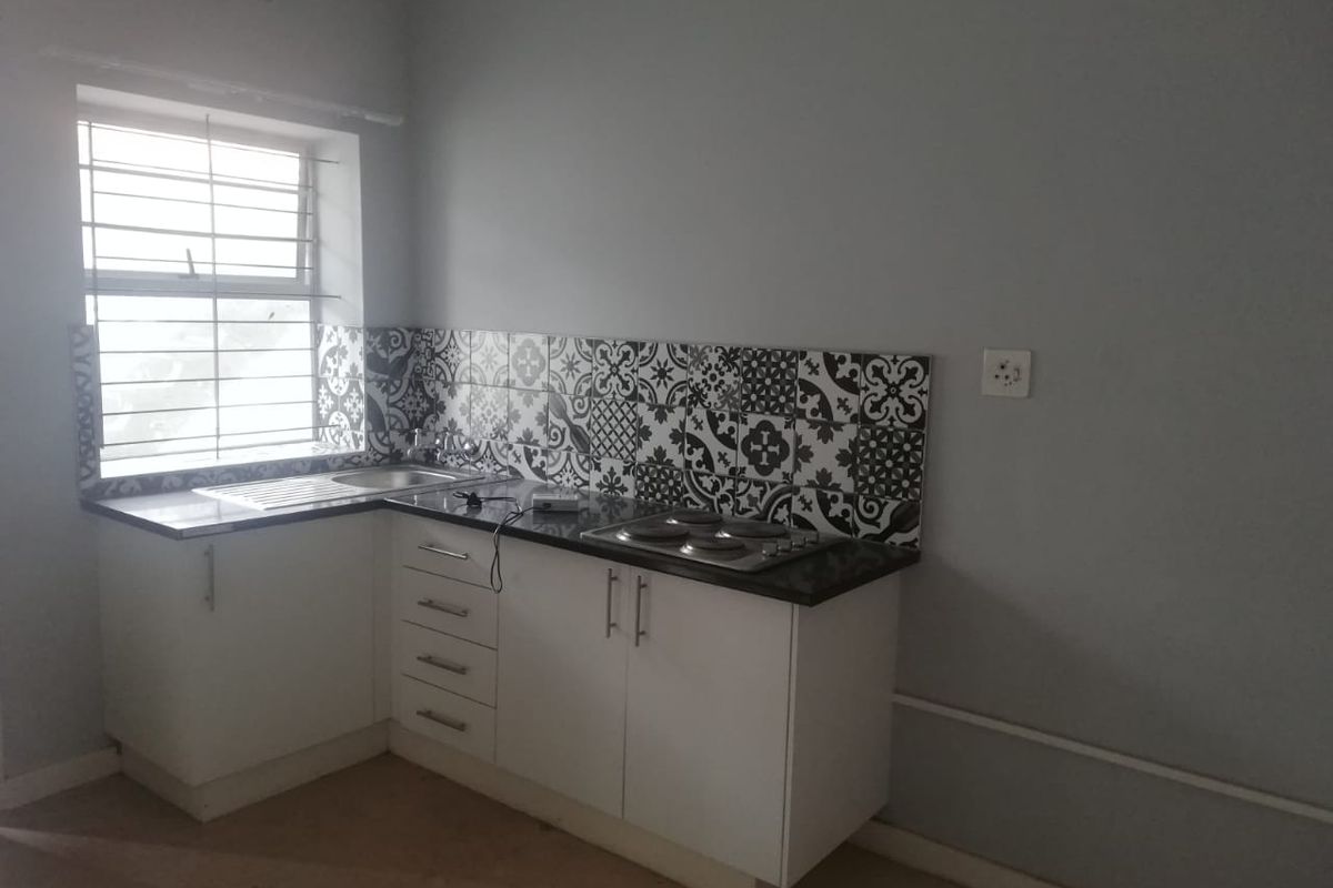 A compact kitchen featuring white cabinetry, dark granite countertops, a patterned tile backsplash, and a built-in electric hob.