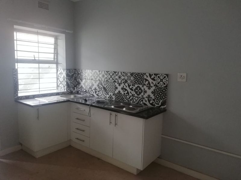A compact kitchen featuring white cabinetry, dark granite countertops, a patterned tile backsplash, and a built-in electric hob.