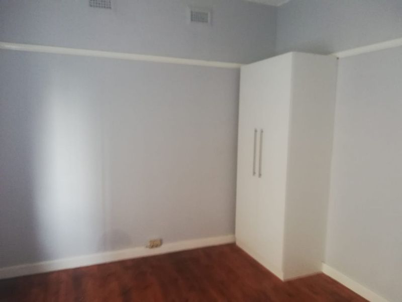 A clean, empty bedroom featuring laminate flooring, a built-in wardrobe, and classic picture rail detailing.