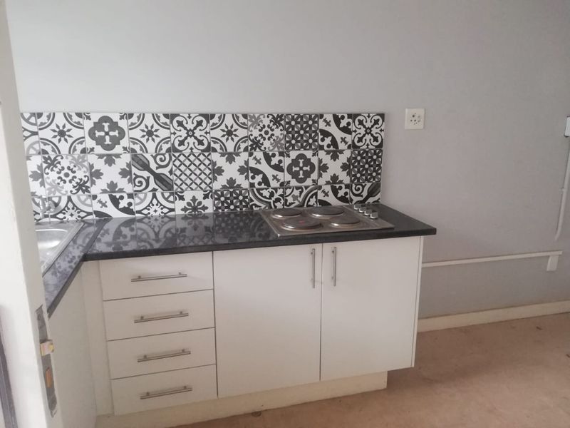A compact kitchen area featuring white cabinetry, a dark granite countertop, an integrated electric hob, and a decorative patterned tile backsplash.