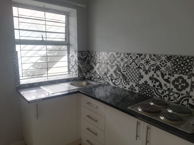 A compact kitchen featuring black granite countertops, patterned tile backsplash, built-in white cabinetry, and an integrated electric hob.