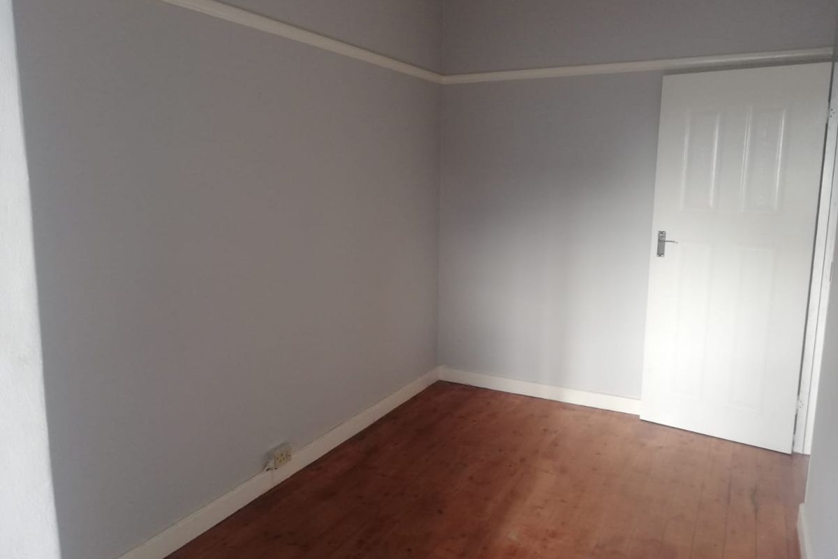 An empty bedroom featuring timber flooring, neutral wall paint, and classic picture rail detailing.