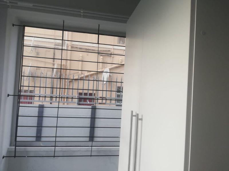 A bedroom interior featuring a white built-in wardrobe and a window fitted with security bars.