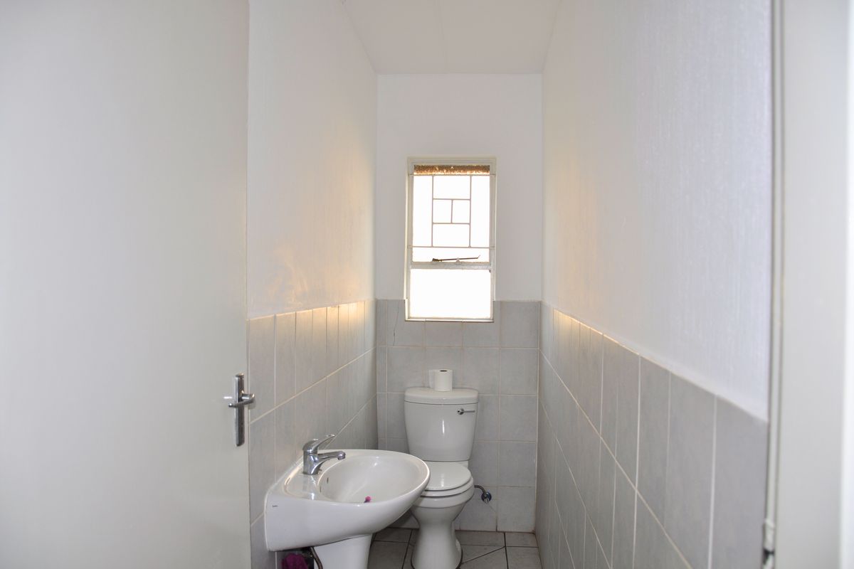 A compact bathroom featuring a pedestal basin, toilet, and neutral wall tiling with a window providing natural light.