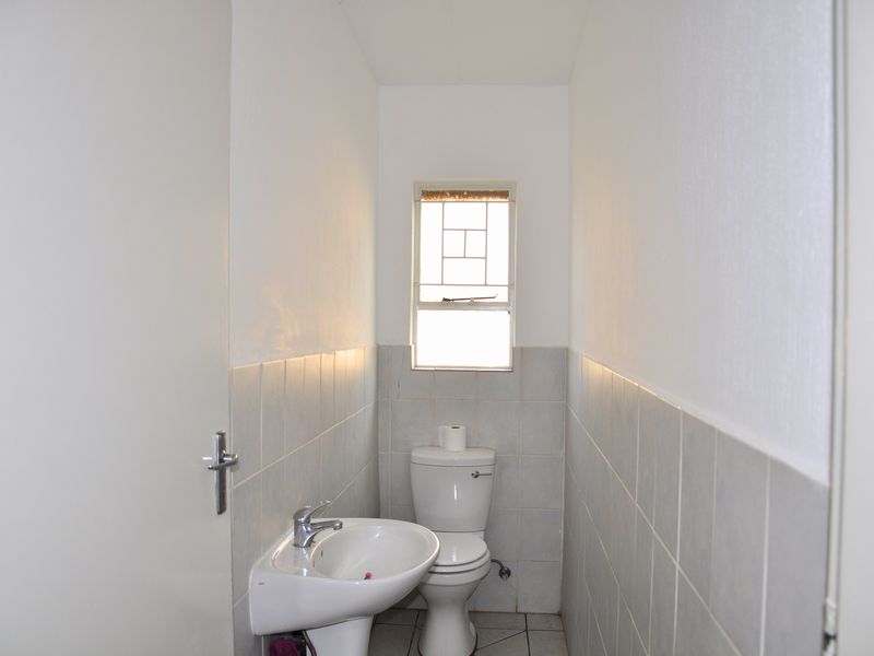 A compact bathroom featuring a pedestal basin, toilet, and neutral wall tiling with a window providing natural light.