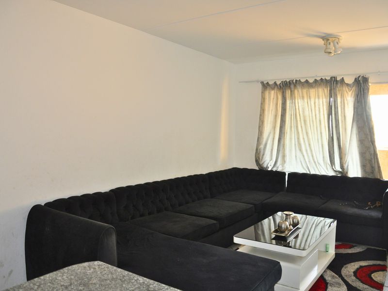 A living room area featuring a large window with curtain rod and ceiling lighting, providing a functional space for relaxation.