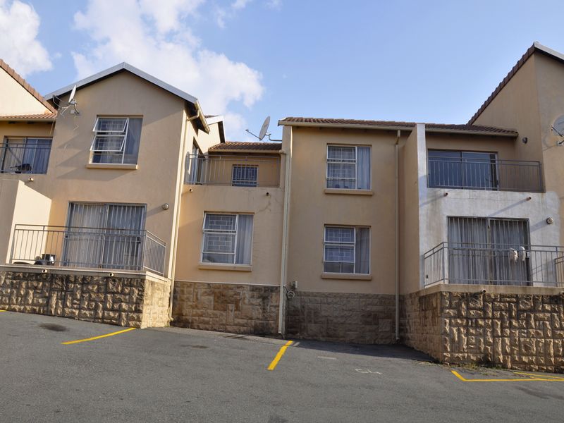 Exterior view of a multi-story apartment complex featuring stone cladding, metal balcony railings, and paved parking area.