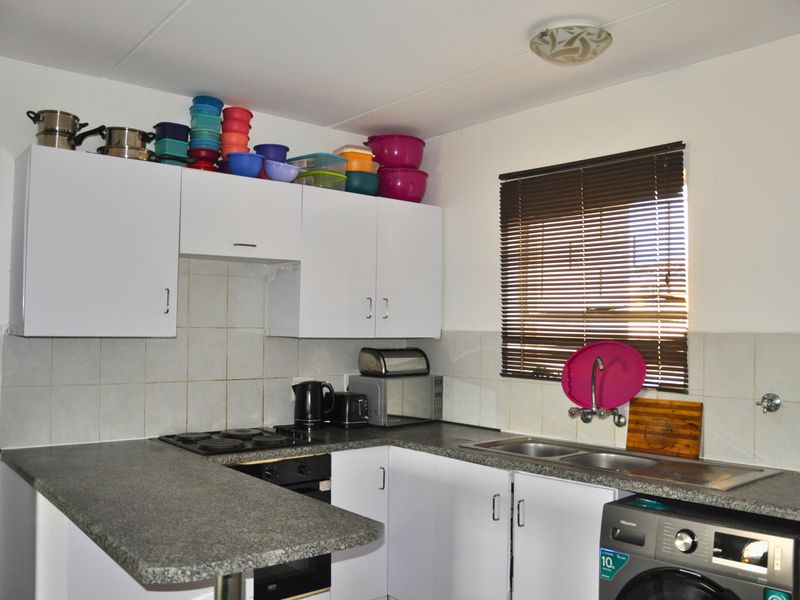 Functional kitchen featuring white cabinetry, laminate countertops, tiled backsplash, built-in oven, electric hob, and a double bowl sink with venetian blinds.