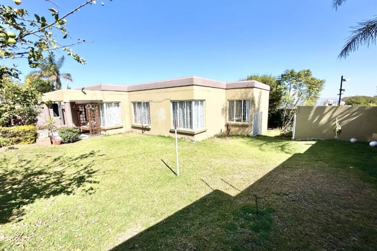 Rear view of the townhouse featuring a private garden, paved patio area, and established lawn with perimeter boundary walls.