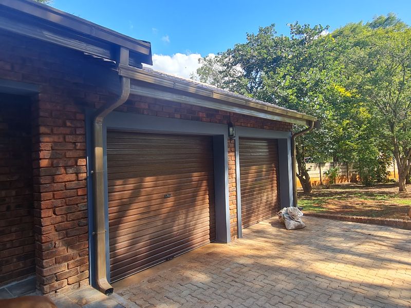 A well-maintained brick exterior featuring a double garage with roller doors and a paved driveway, set against a landscaped garden.