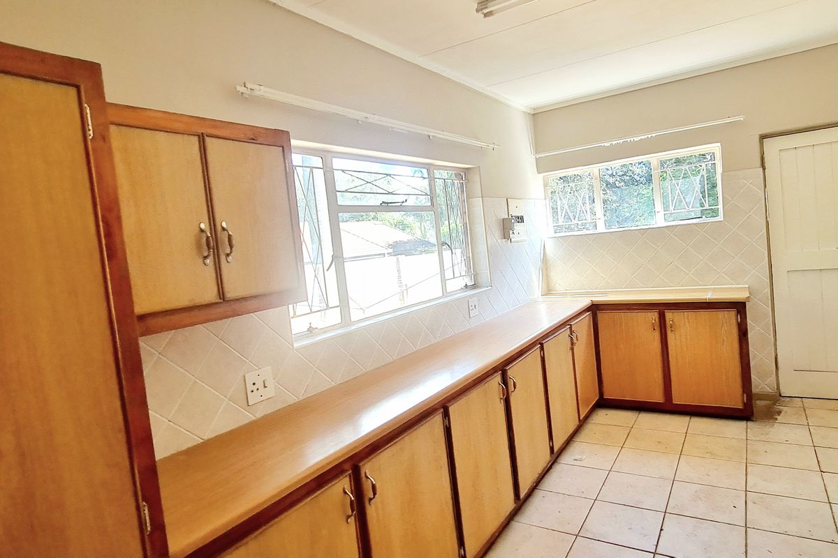 A functional kitchen featuring wooden cabinetry, laminate countertops, tiled backsplash, and a built-in electric hob, offering a blank canvas for renovation.