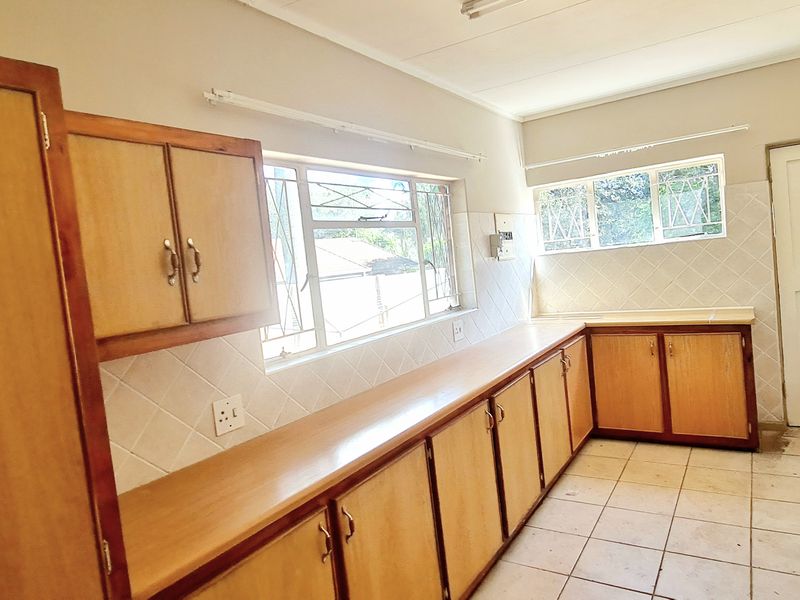 A functional kitchen featuring wooden cabinetry, laminate countertops, tiled backsplash, and a built-in electric hob, offering a blank canvas for renovation.